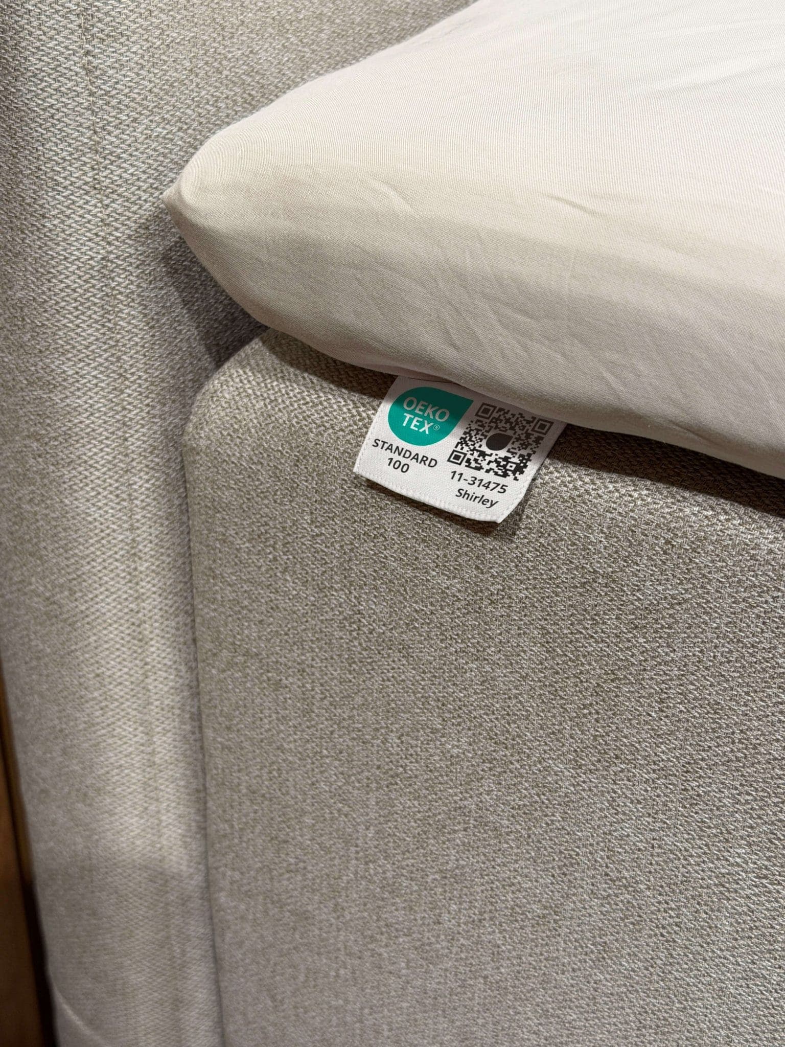 Metka OEKO-TEX® STANDARD 100 przyszyta do beżowej tkaniny łóżka pod prześcieradłem