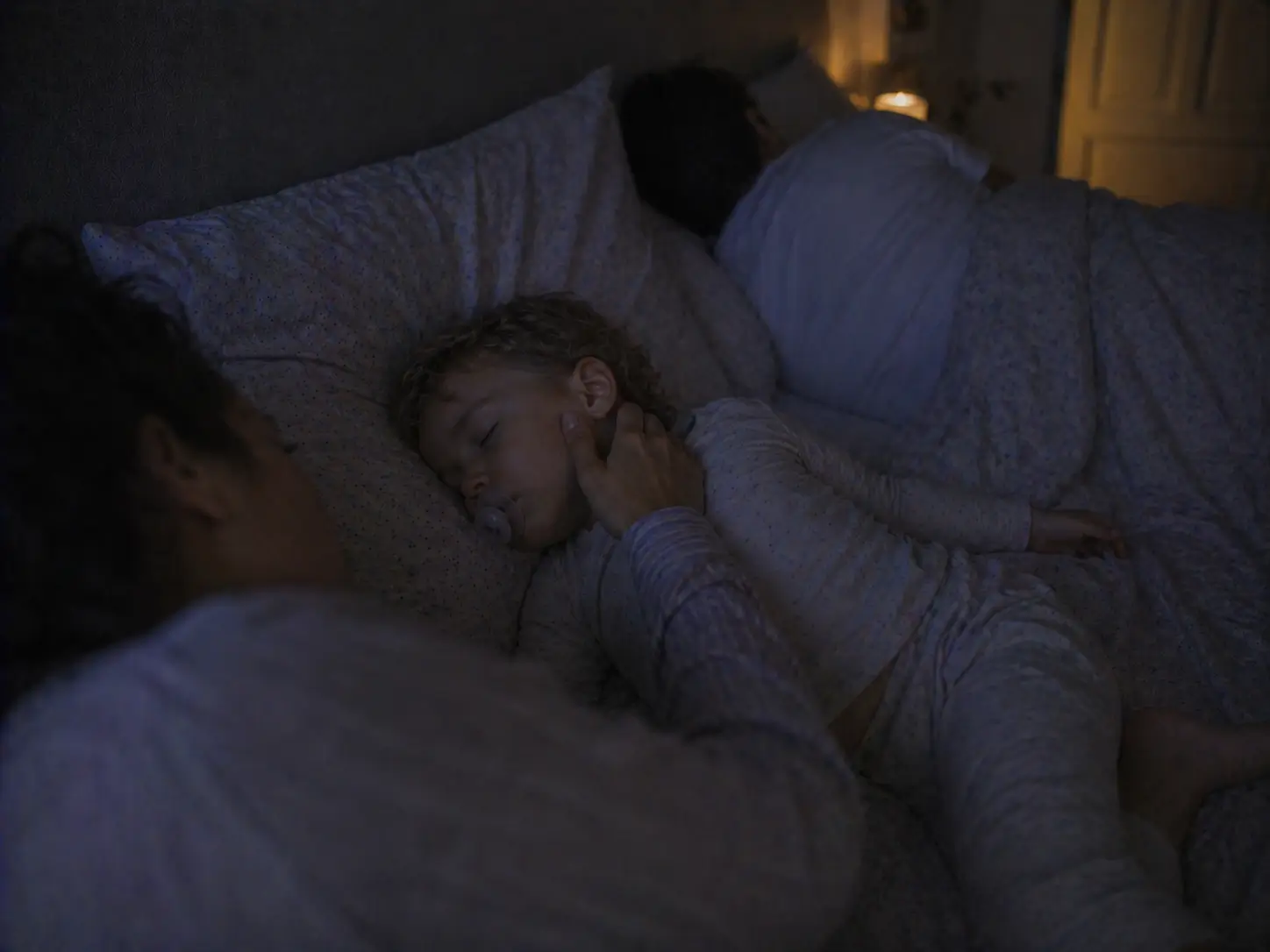 Mama delikatnie dotyka policzka śpiącego dziecka w szerokim łóżku rodzinnym nocą