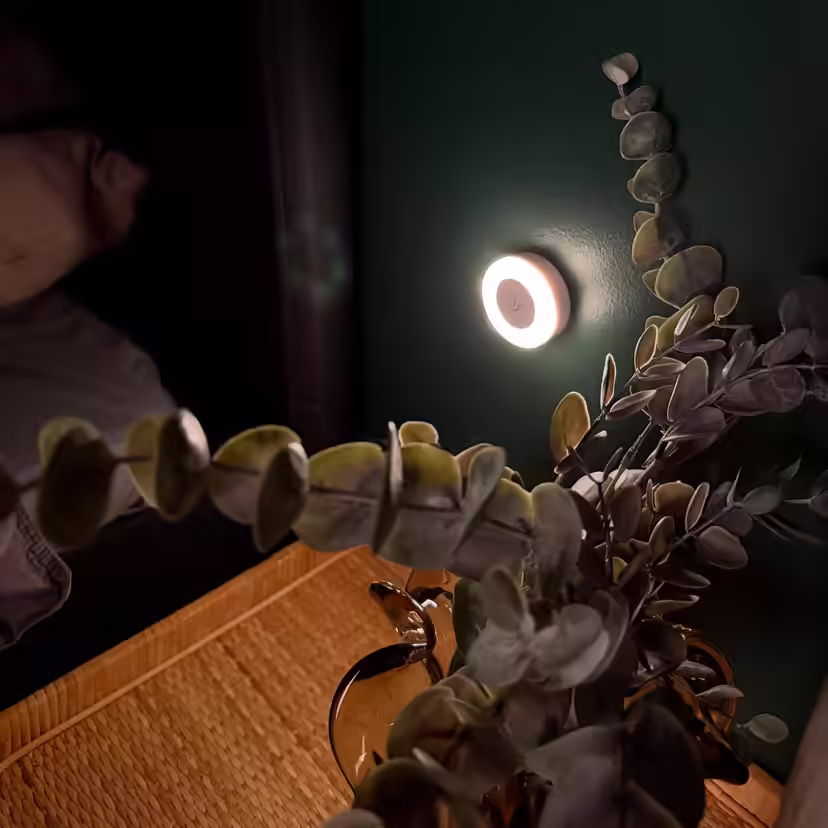 Okrągła lampka do karmienia piersią, rzucająca nocą delikatne światło na ścianę przy łóżku
